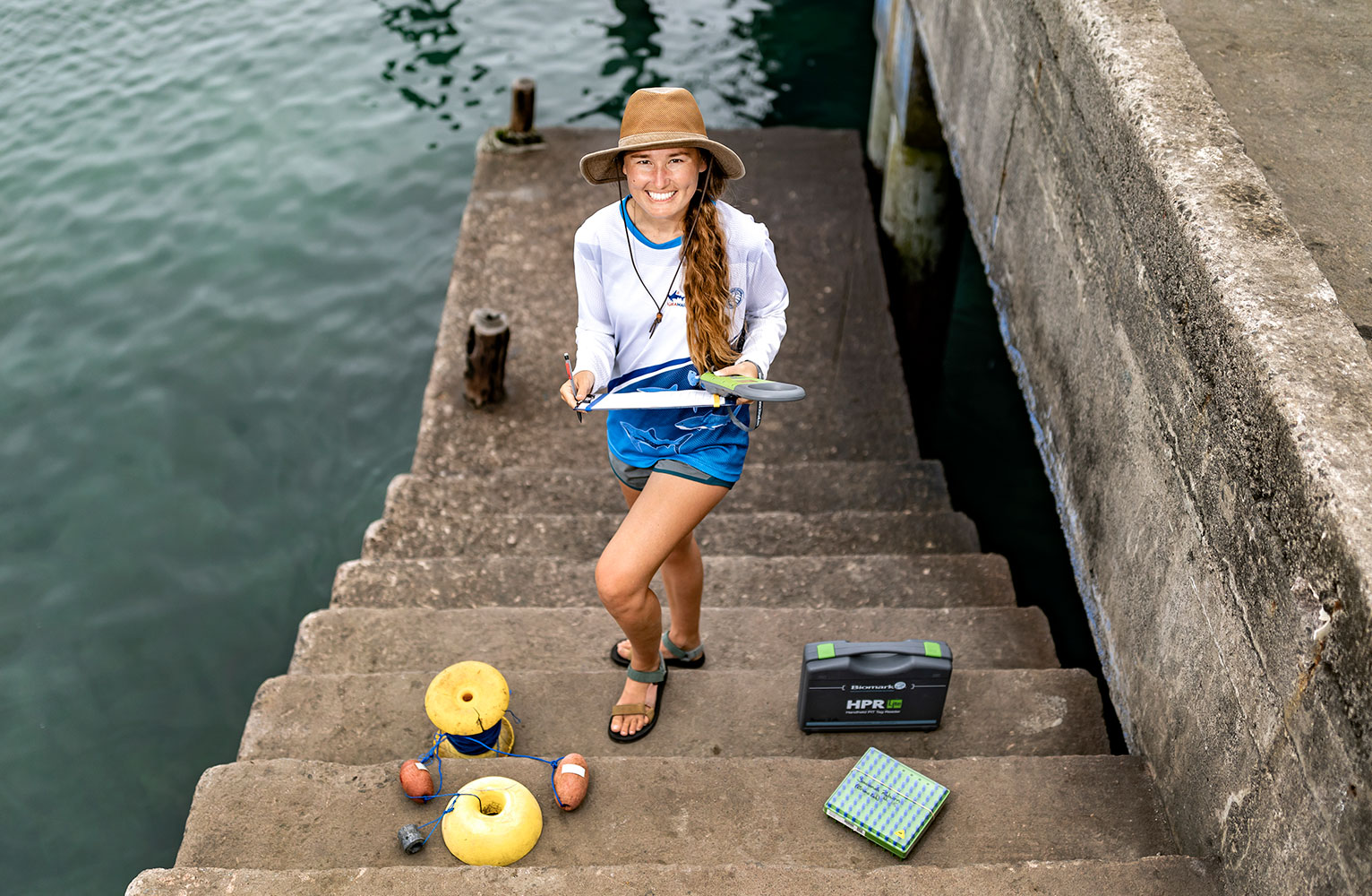 Savannah Rayburn poses on steps leading down to ocean, holding a specimen tray