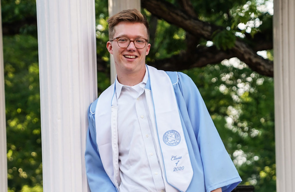 Cole Mueller poses in front of the Old Well in a cap and gown