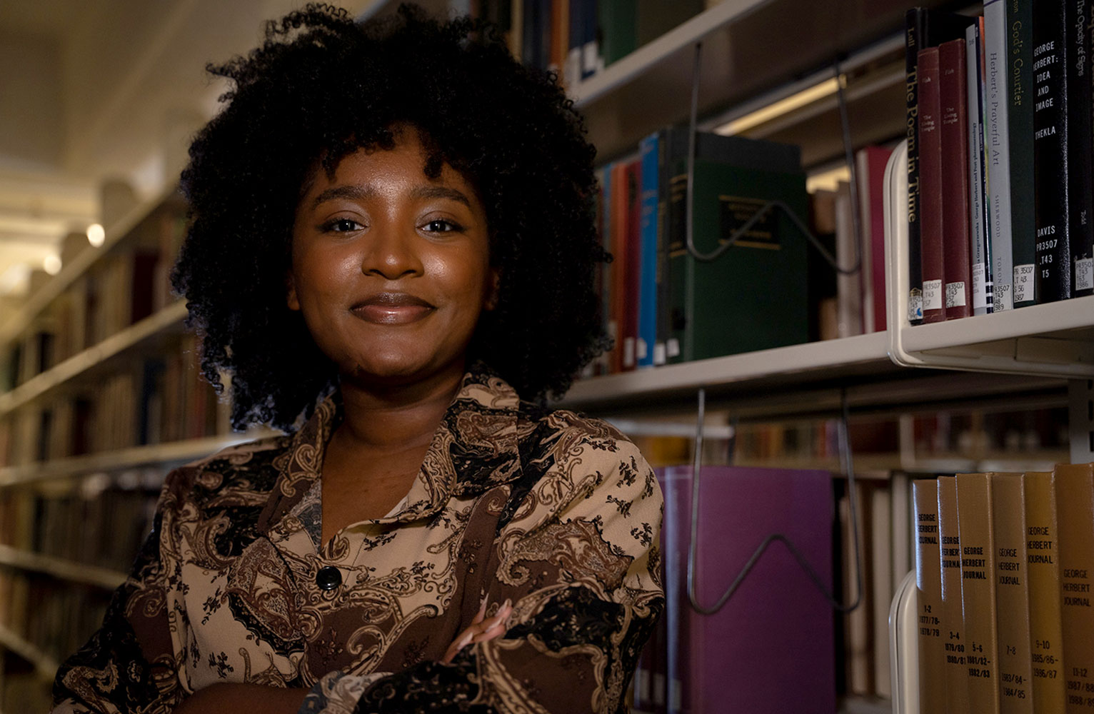 A portrait of Ayana Monroe in a library in front of books.