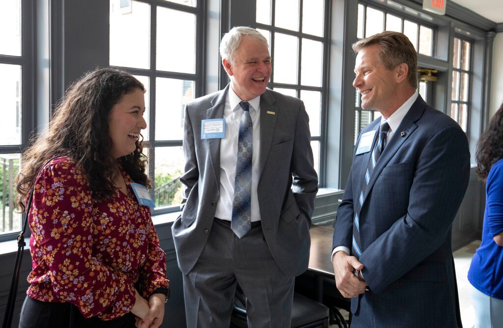 Ana Zurita Posas, Scott Hamilton, and Kevin Guskiewicz stand chatting at the GoldenLEAF Luncheon.