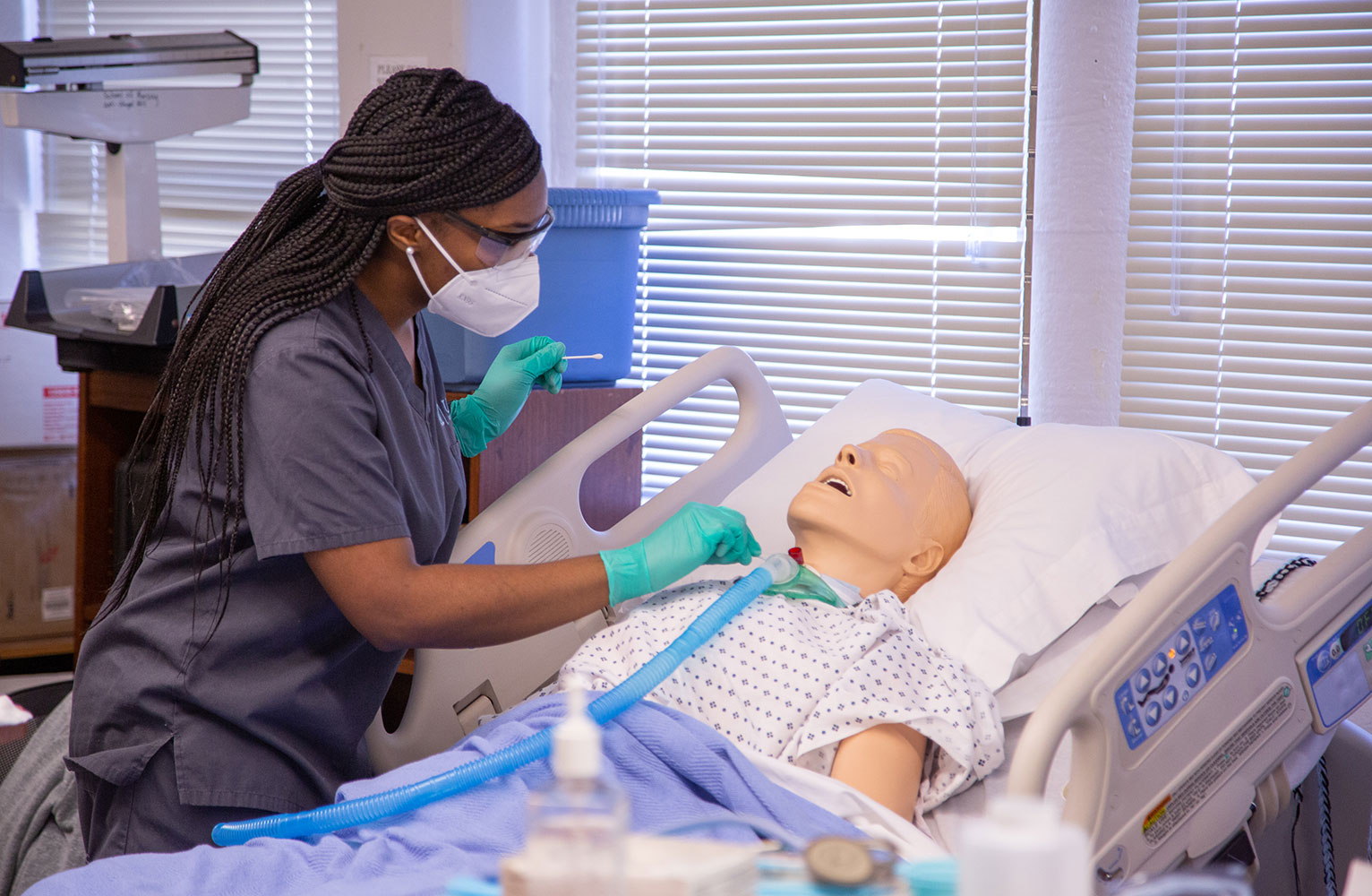 A nursing student leans over a dummy in a simulated training environment