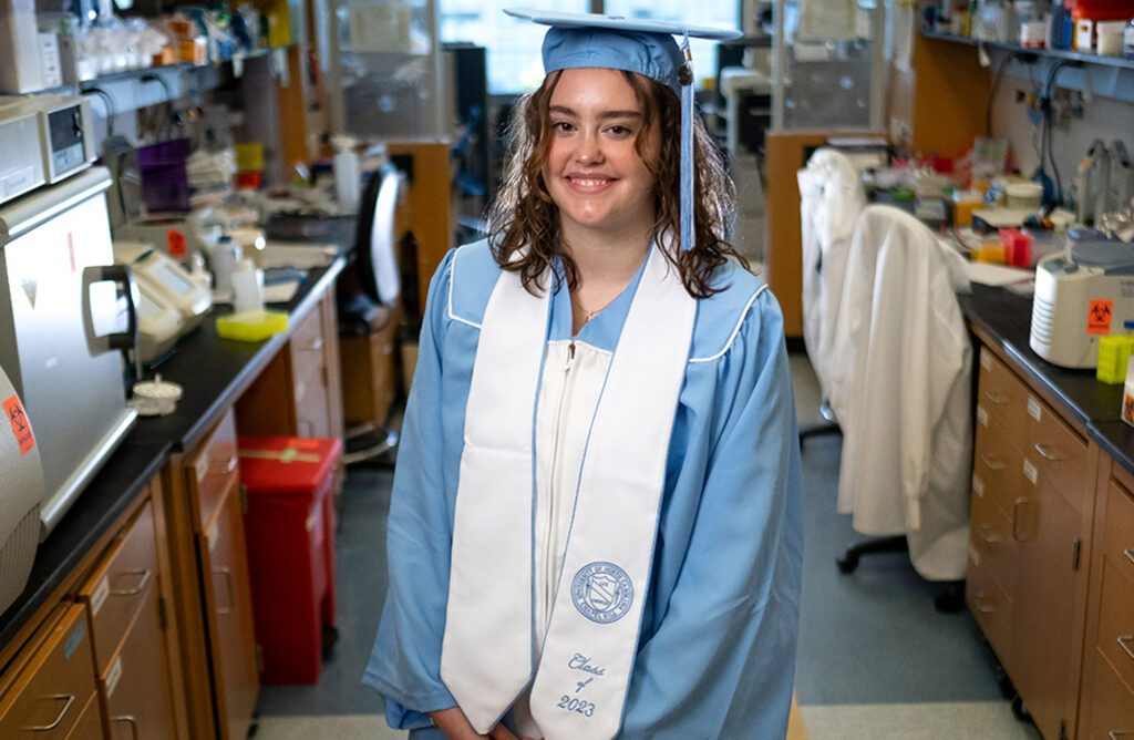 Abigail Rohy stands in a lab in her graduation regalia