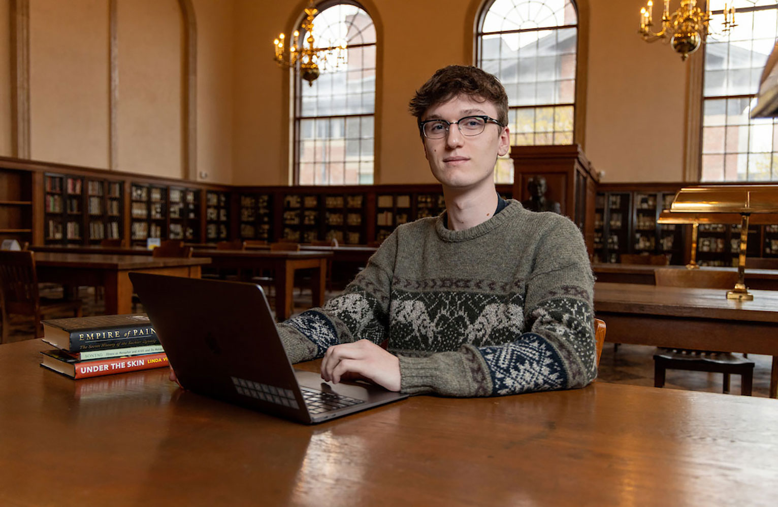 Sonny Griffith sits a a table in Wilson Library while typing on a laptop while looking at the camera. 