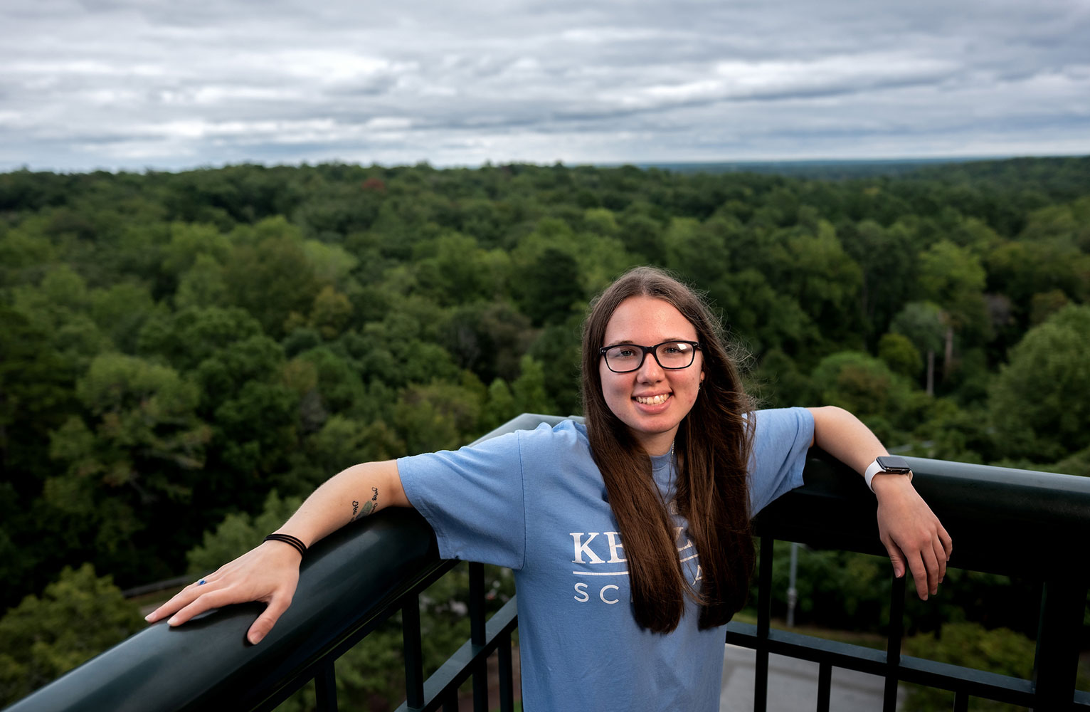 Kessler Scholar Emily Shipway stands on a rooftop leaning against a railing with trees and sky in the background
