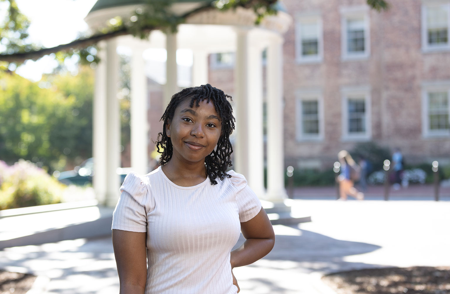 Carolina Covenant Scholar Nya Smythe faces the camera with the Old Well at UNC-Chapel Hill in the background