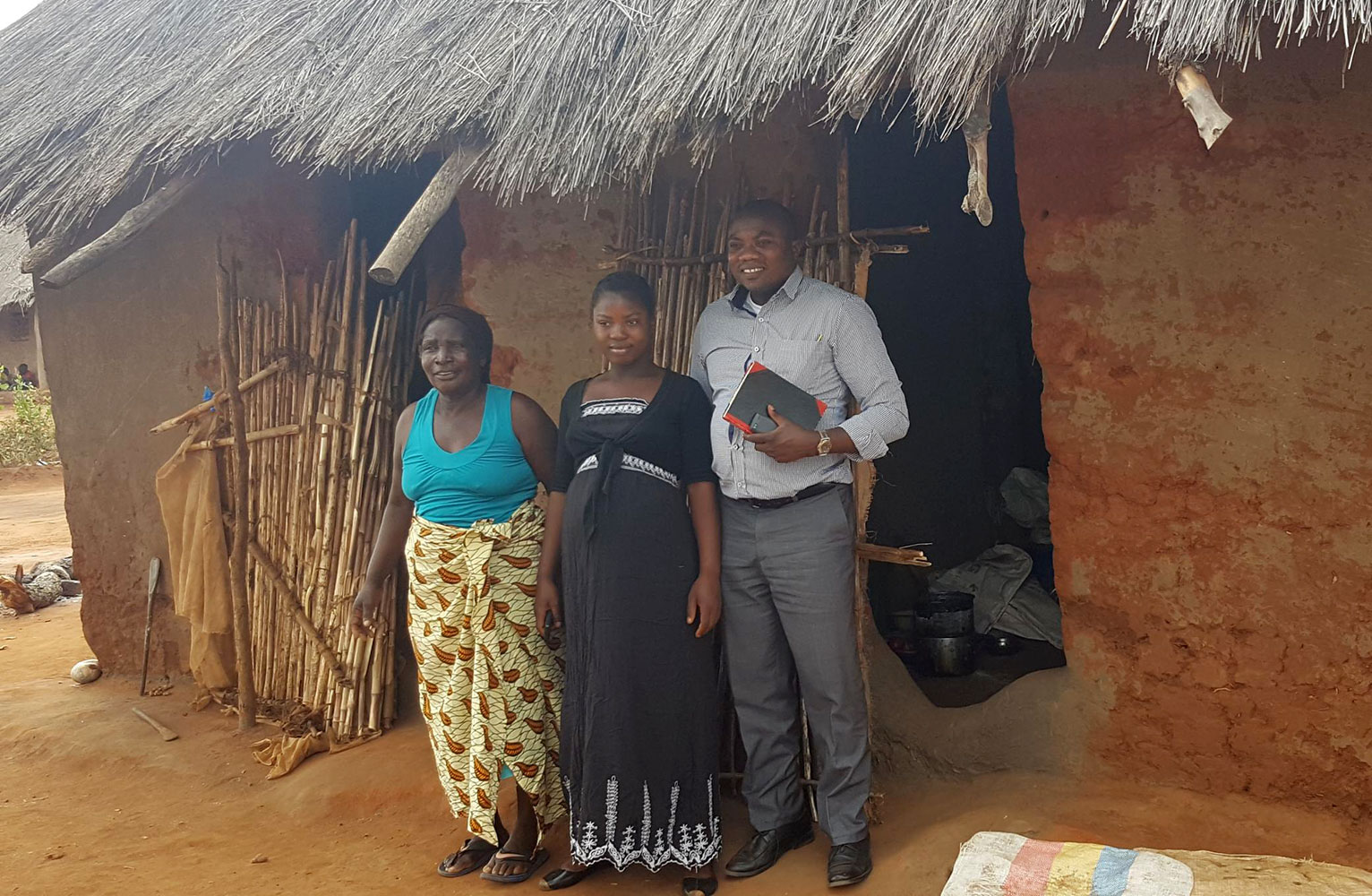 Mathias Zimba stands with two mothers in front of a home in rural Zambia